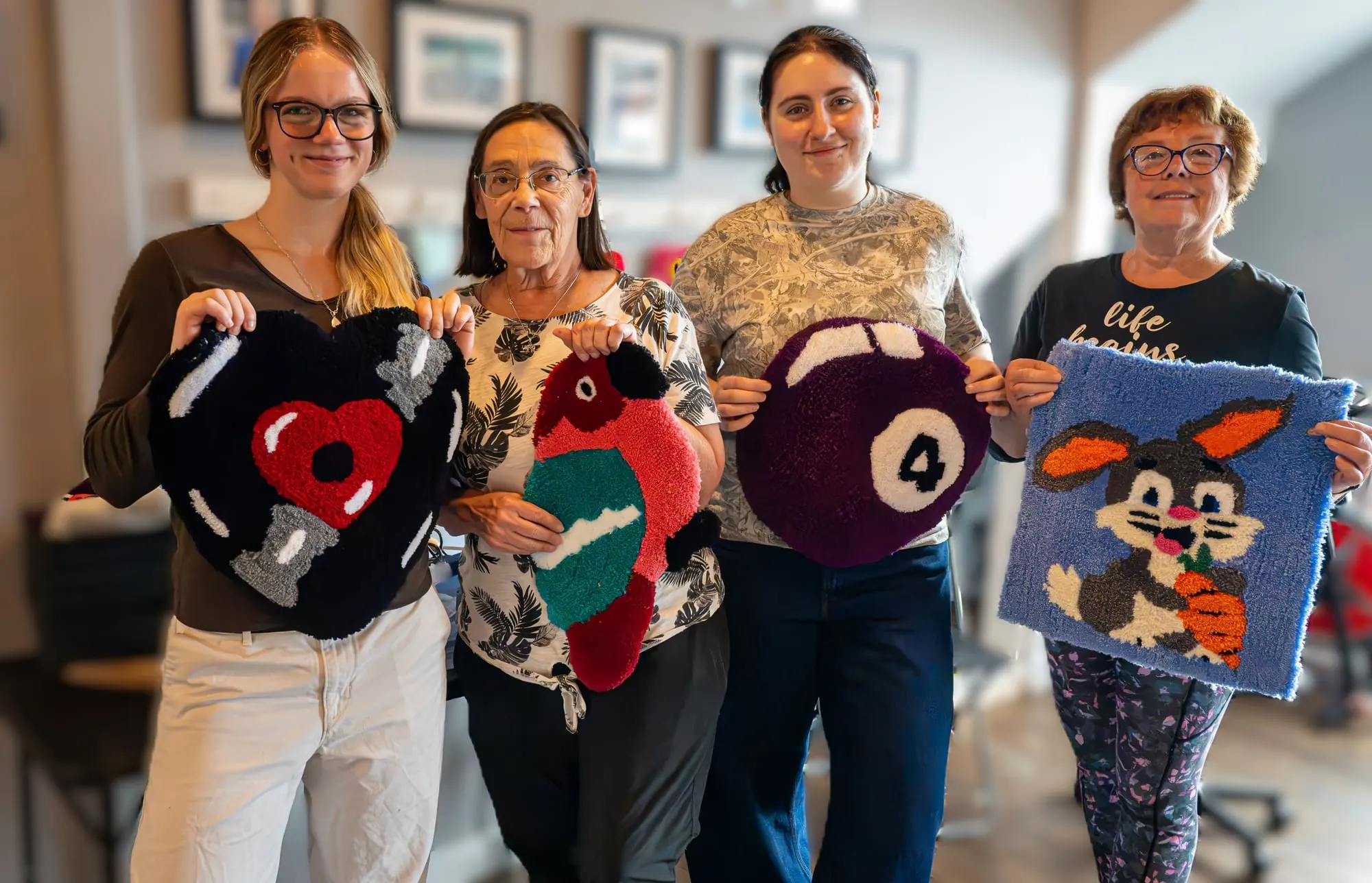 Quatre participantes fières de leurs tapis tuftés en atelier
